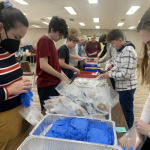 Scouts in Chicago stand and form an assembly line for efficient packing of Pocket First Aid Kits